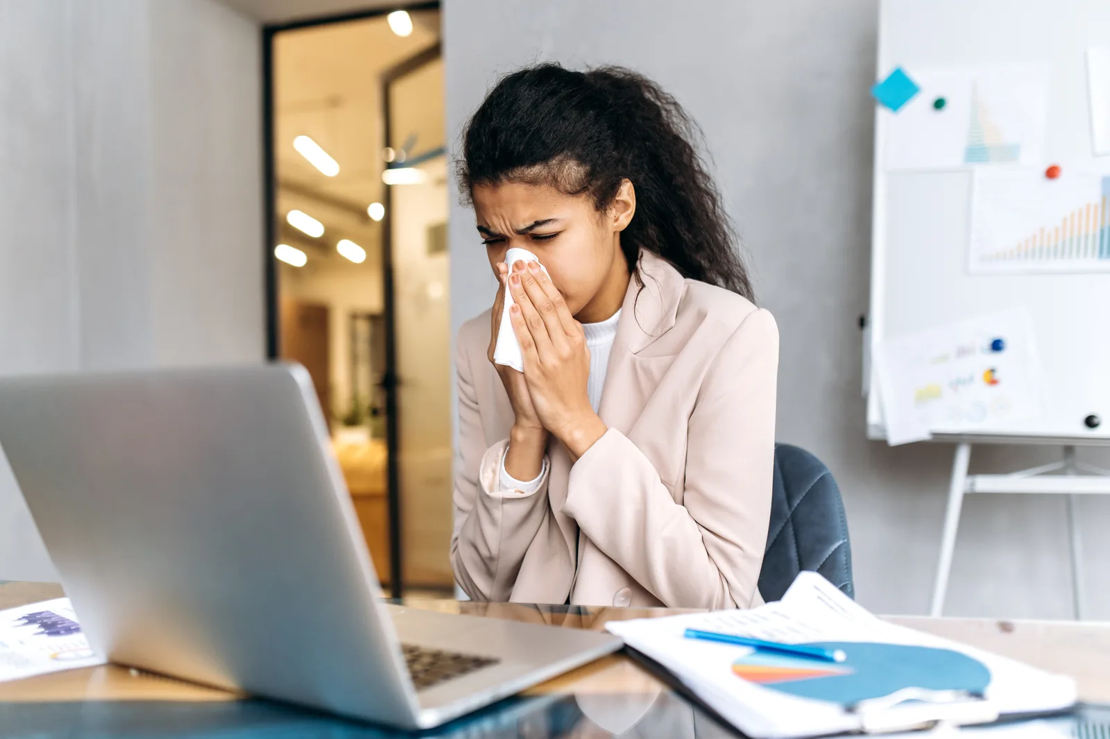 Salariée enrhumée se mouchant à son poste de travail, illustrant un arrêt de travail